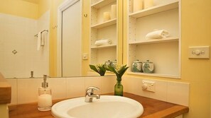A bathroom with a white sink, a mirror, and shelves with toiletries.