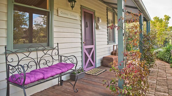 A porch with a metal bench, a purple door, and a sign reading 'Quince Cottage.'