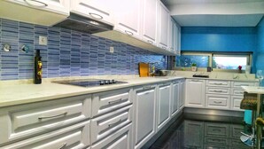 A modern kitchen with white cabinets, a blue-tiled backsplash, a built-in stove, and a window with a view.