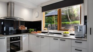 A modern kitchen with a built-in oven, a coffee machine, and a window with a view of a garden.