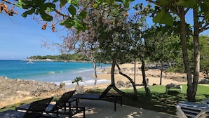 Eine Terrasse am Strand mit Liegestühlen und einem Tisch, mit Blick auf einen Sandstrand und das Meer.