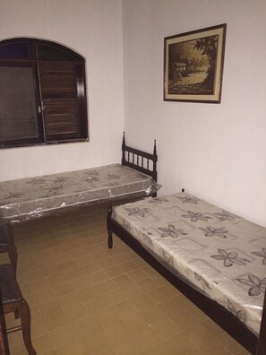 A small room with two single beds, a wooden chair, a window with shutters, and a framed picture on the wall. - Nature and Welfare (Sete Barras)