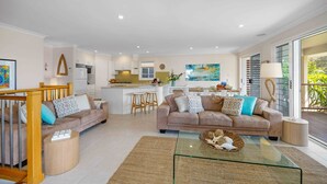 A spacious living area with two sofas, a glass coffee table, and a kitchen in the background. - Allure by the Sea - beachfront luxury home (Bonny Hills)