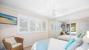 A bedroom with a bed, a chair, a ceiling fan, and a large window with blinds. - Allure by the Sea - beachfront luxury home (Bonny Hills)