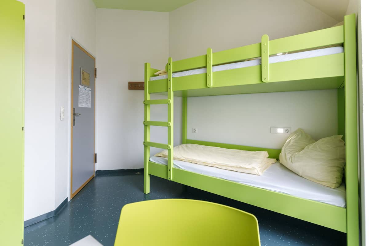 Ein Schlafraum mit Etagenbett, einer Leiter, einer Tür mit Schild und einem gelben Stuhl.