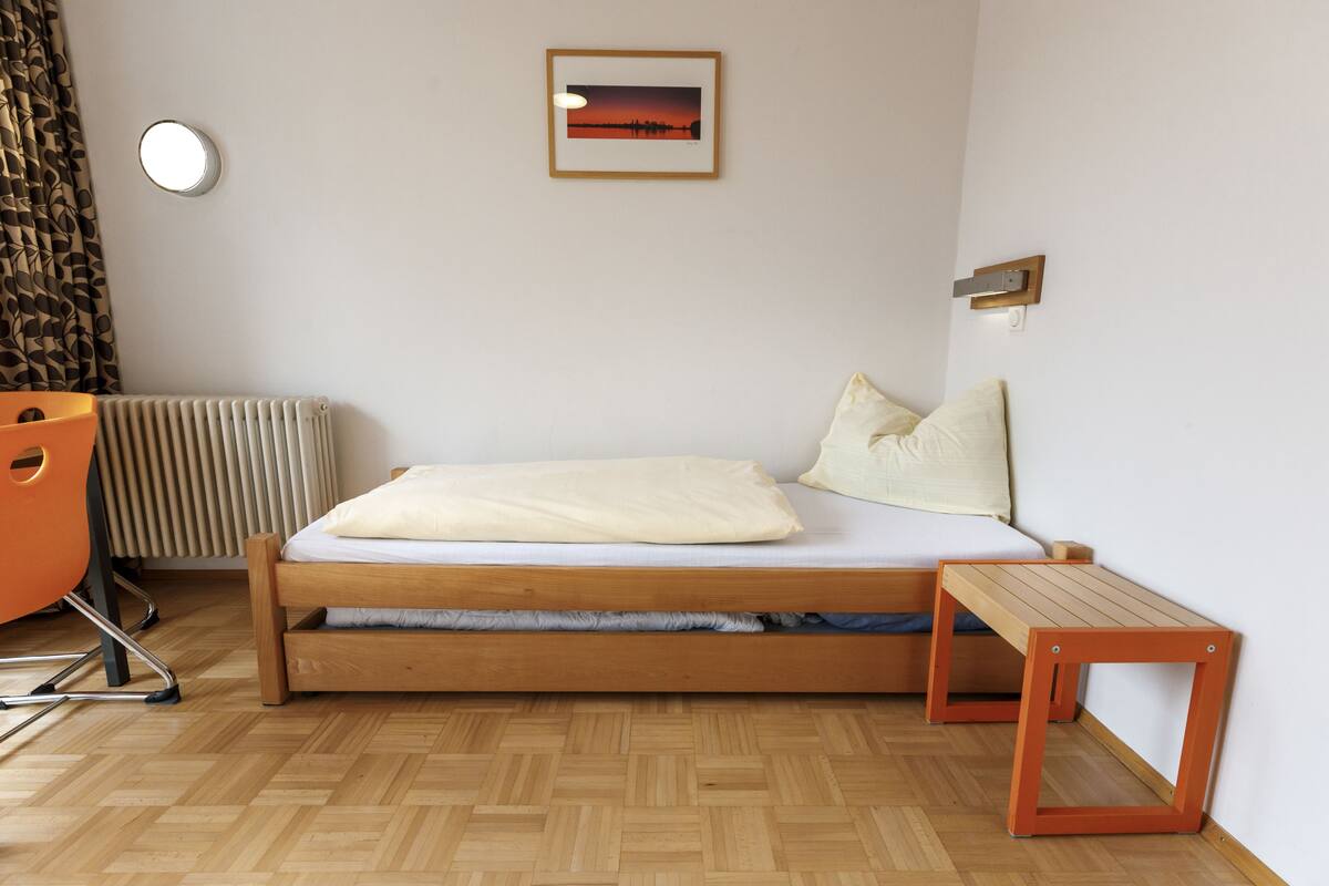 Ein Schlafzimmer mit Bett, Nachttisch, Stuhl, Heizkörper und einem Bild an der Wand.