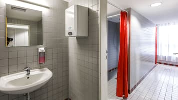 Un baño con lavamanos blanco, un espejo, un secador de manos y una cortina de ducha.