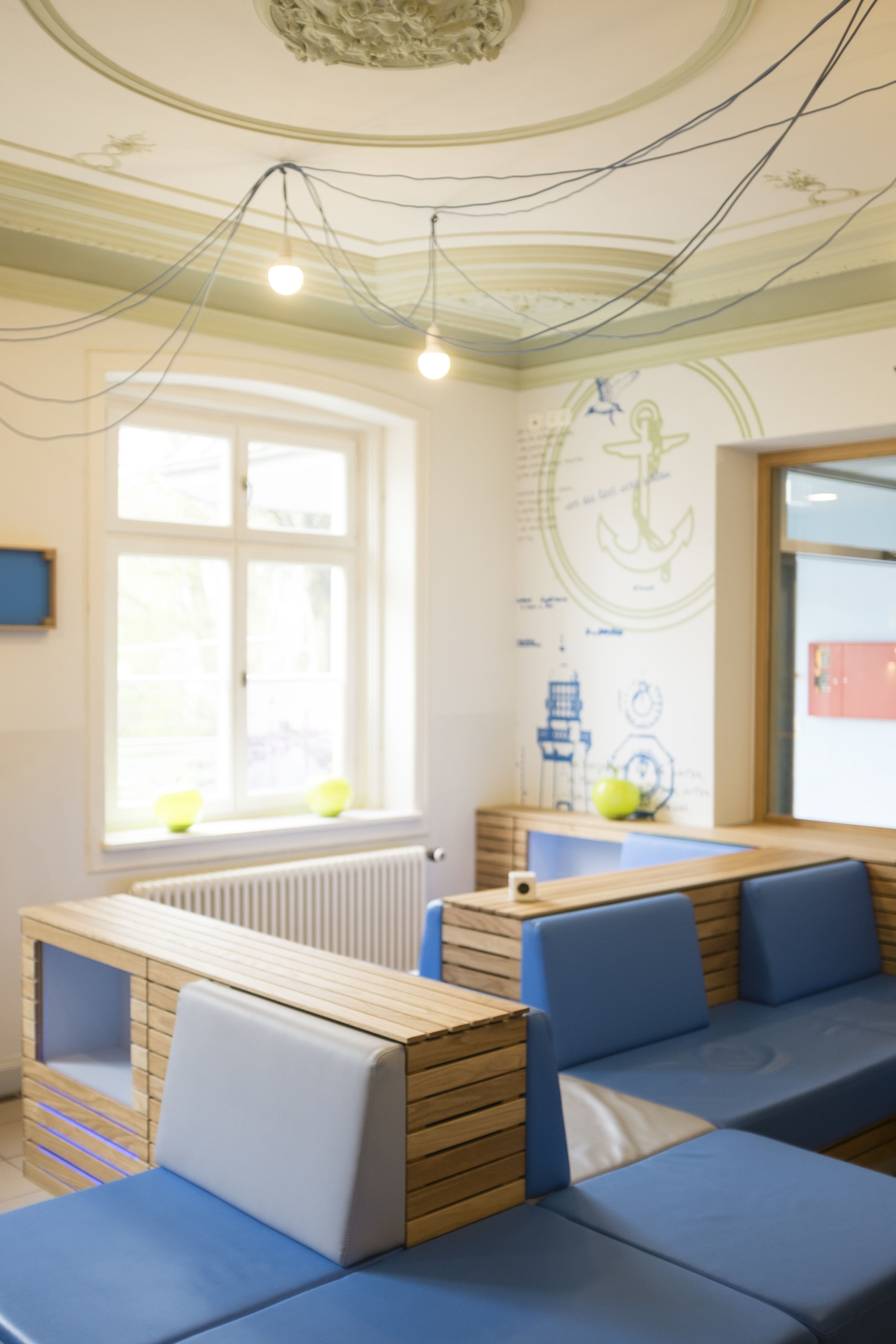 Une pièce comprenant un banc en bois servant de coin salon, une fenêtre avec des stores et un mur décoré d’œuvres d’art sur le thème de la marine.