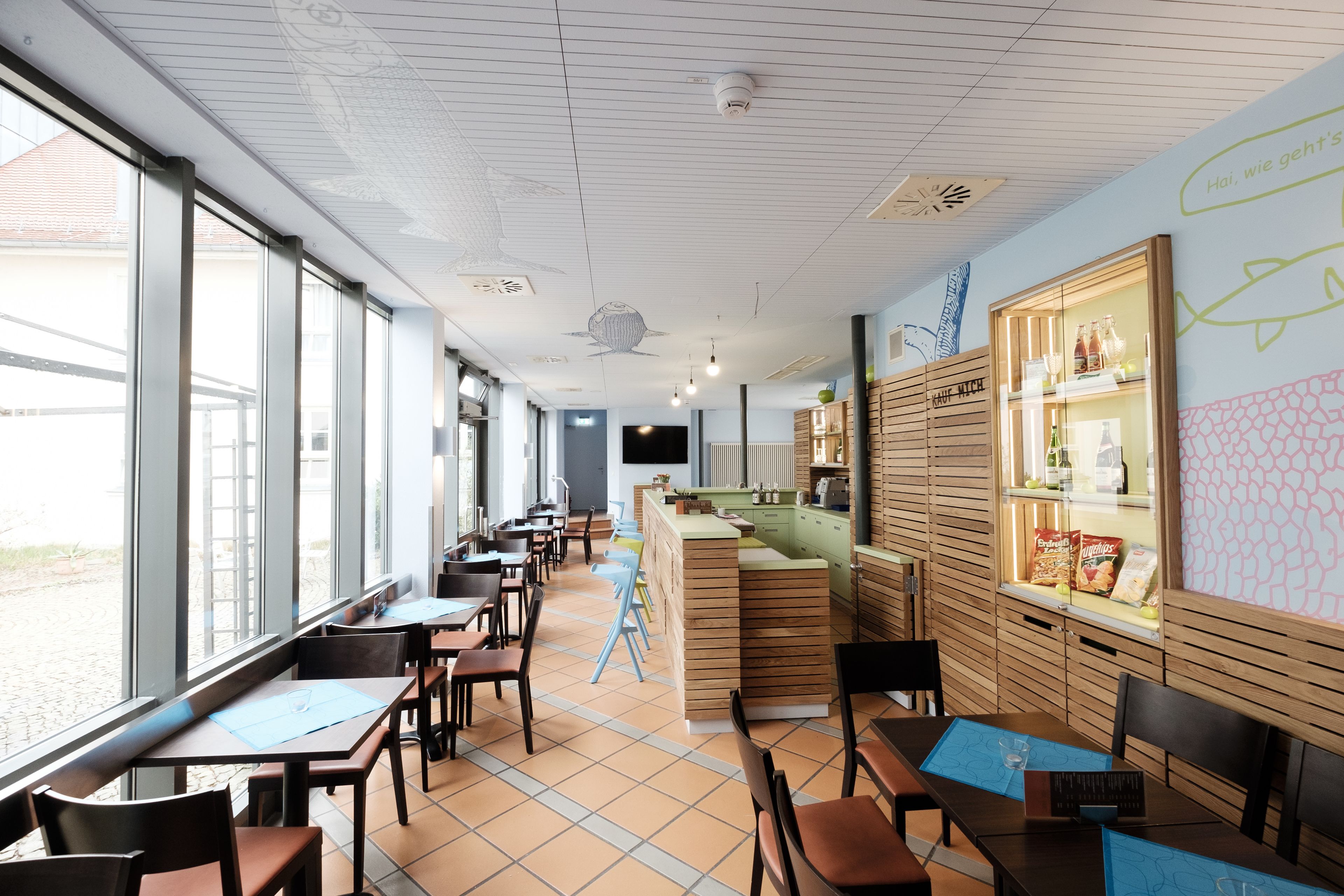 Un restaurante con una decoración moderna, que cuenta con mobiliario de madera, una barra con la carta y grandes ventanales con vistas al exterior.