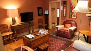 A living room with a wooden desk, television, leather armchair, and a red patterned rug. - Cafe Spa Suite 1 bedroom (North Adelaide)