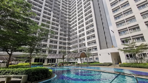A high-rise residential building with a swimming pool and surrounding greenery.