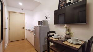 A compact kitchen with a refrigerator, microwave, and a small dining table set with cups and a vase of flowers.