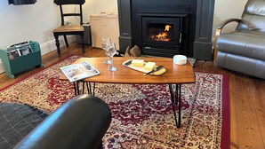 A cozy living room with a fireplace, a wooden coffee table, a leather armchair, and a patterned rug. - Cosy Heritage Cottage in Newstead, Central to Daylesford, Maldon & Castlemaine (Newstead)