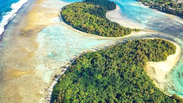Vista aérea de una isla tropical con aguas turquesas cristalinas, playas de arena y vegetación verde exuberante.