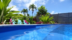 Una piscina con agua azul cristalina, rodeada de plantas verdes y una valla de madera.