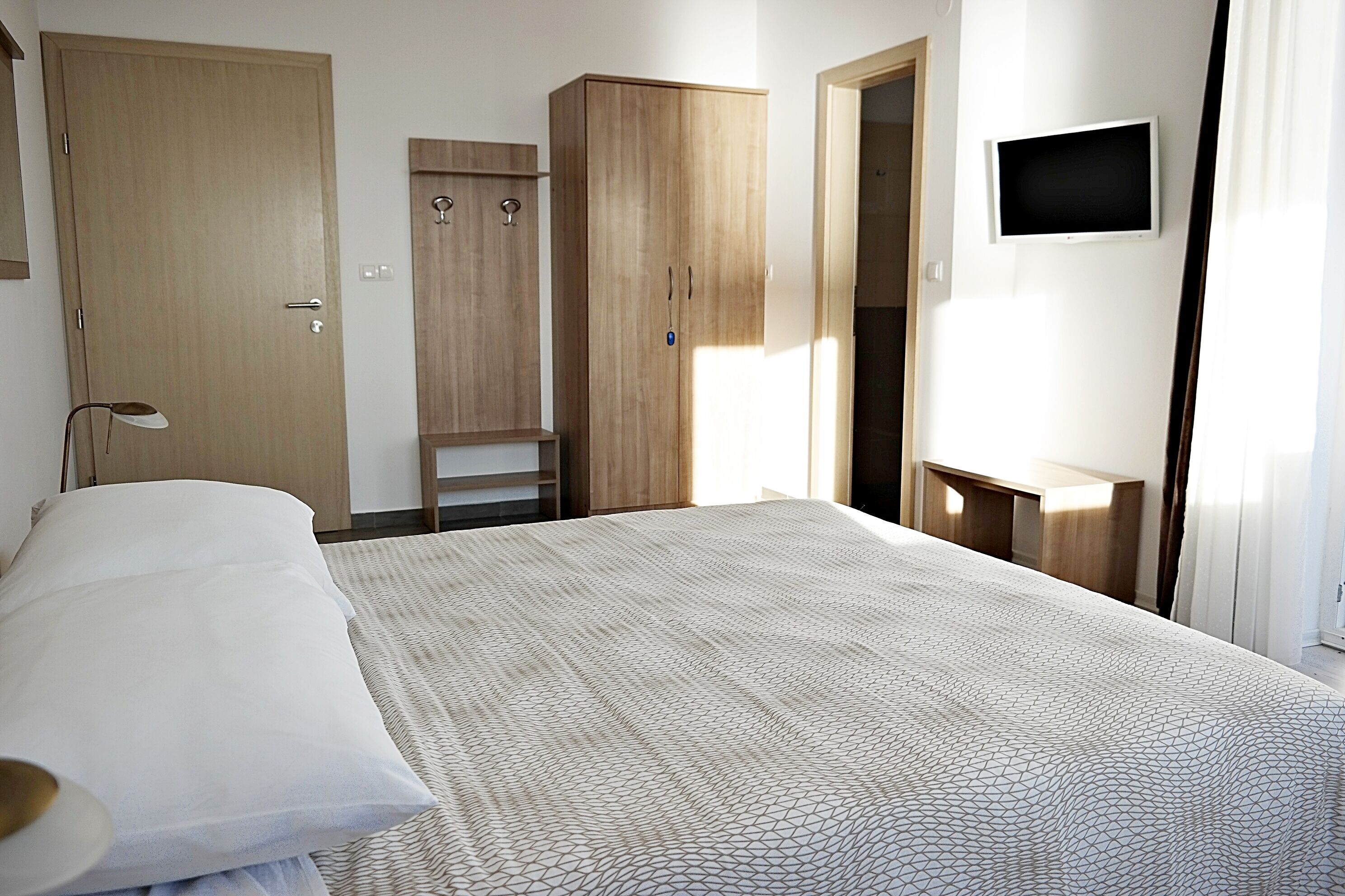 A bedroom with a bed, wooden wardrobe, a TV mounted on the wall, and a small table.