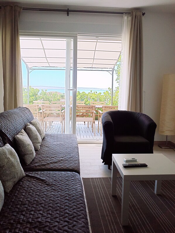 A room with a sofa, a chair, a coffee table, and a view of an outdoor patio with tables and chairs.
