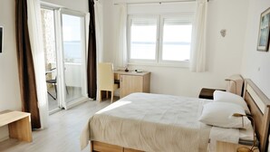Een slaapkamer met een bed, een bureau, een stoel en uitzicht op de zee door een raam.