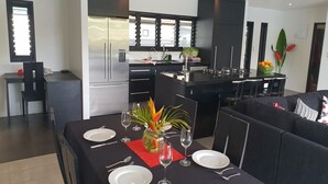 A modern kitchen with a central island, a dining area with a table set for four, and a sofa in the living area. - Boaza Place is situated in Nikao and offers an outdoor swimming pool.  (Puapuautu Tapere)