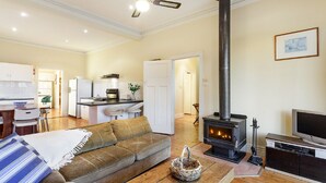 A cozy living room with a sofa, a TV, and a fireplace. There is a kitchen area with a refrigerator and a dining table. - Woolamai Park Suits 2-3 Families LARGE 7 Bedrooms (Woolamai)