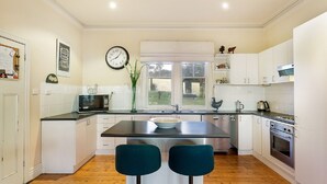 A modern kitchen with white cabinets, a black countertop, a stainless steel sink, and a double oven. There is a clock on the wall and a window with a view of the outdoors. - Woolamai Park Suits 2-3 Families LARGE 7 Bedrooms (Woolamai)