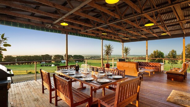 An outdoor dining area with wooden tables and chairs, a barbecue grill, and a view of the countryside. - Woolamai Park Suits 2-3 Families LARGE 7 Bedrooms (Woolamai)
