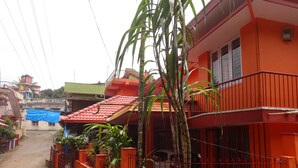 A residential area with a red building, a covered area with a blue tarp, and a narrow street. - For delightful stay, visit us (Madikeri)