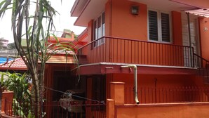 A two-story building with a red exterior, a balcony with a red railing, and a small window with a sign above it. - For delightful stay, visit us (Madikeri)