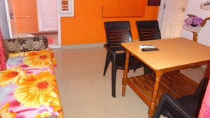 A room with an orange wall, a wooden table with two chairs, a sofa with floral upholstery, and a door with a window. - For delightful stay, visit us (Madikeri)