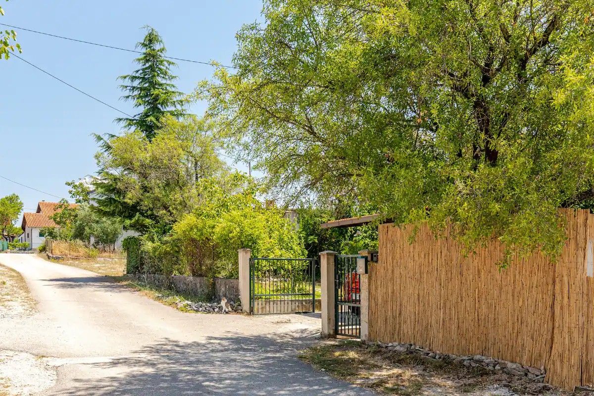 A rural road with a gated entrance, surrounded by trees and a wooden fence.