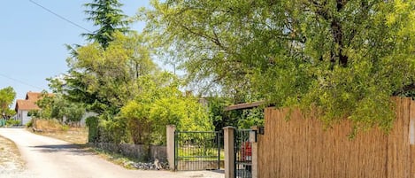 A rural road with a gated entrance, surrounded by trees and a wooden fence.