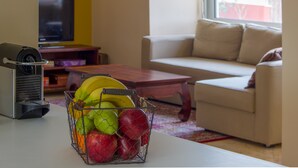 Uma sala de estar com um sofá branco, uma mesa de centro e uma cesta de frutas contendo bananas e maçãs.