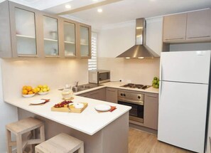 A modern kitchen with a central island, stainless steel appliances, and wooden cabinets. - Sound of Waves on Bondi (Bondi Beach)