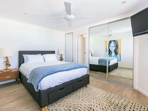 A modern bedroom with a bed, bedside tables, a ceiling fan, and a large mirror. - Sound of Waves on Bondi (Bondi Beach)