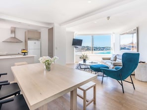 A modern living space with a dining area, a sofa, a TV, and a view of the beach. - Sound of Waves on Bondi (Bondi Beach)
