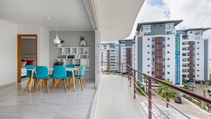 Ein modernes Apartment mit Balkon, einem Essbereich mit blauen Stühlen und Blick auf die umliegenden Gebäude.