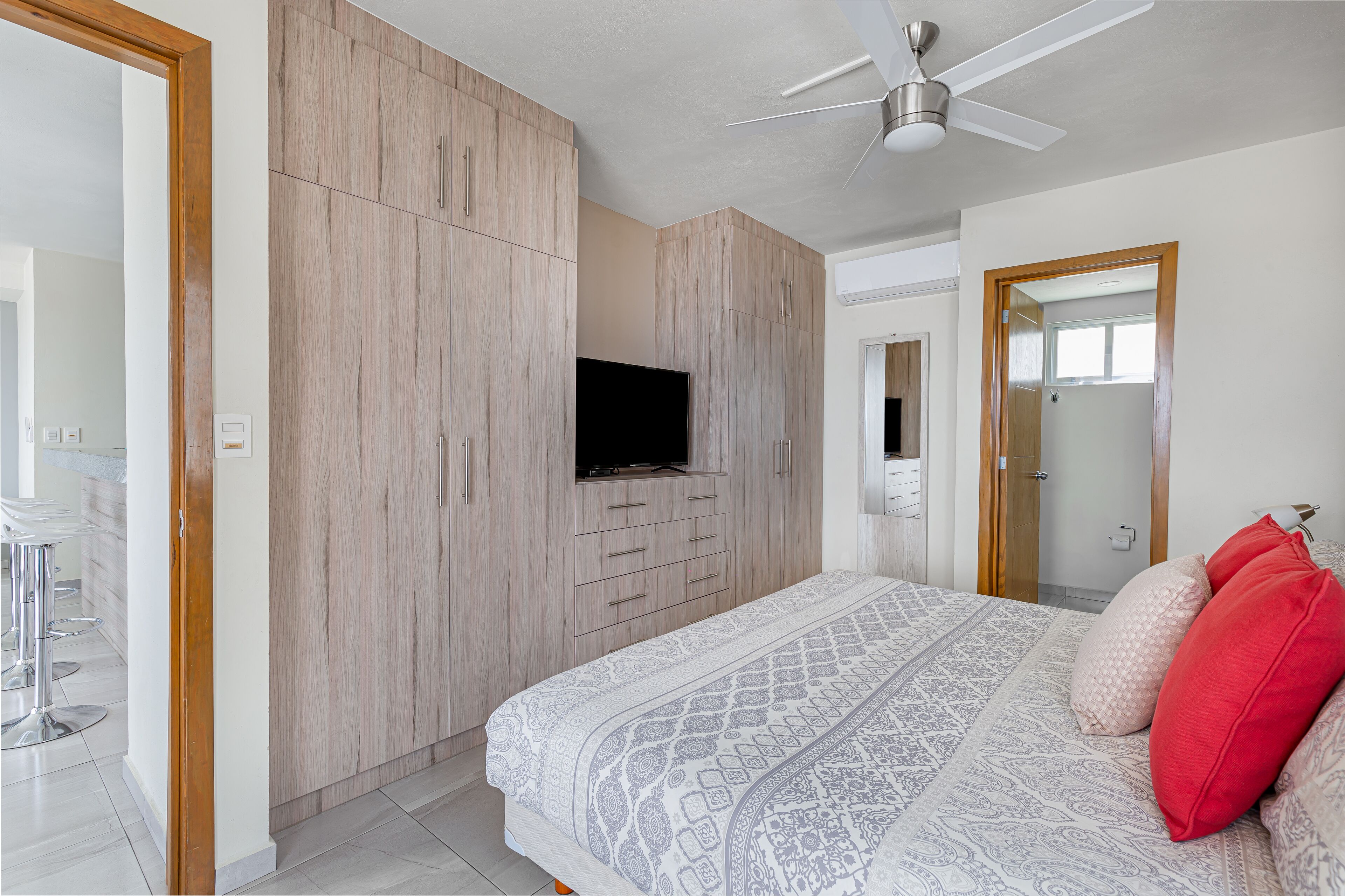 A bedroom with a bed, a TV mounted on the wall, and a ceiling fan.