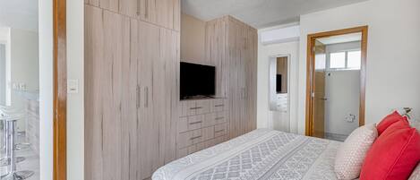 A bedroom with a bed, a TV mounted on the wall, and a ceiling fan.