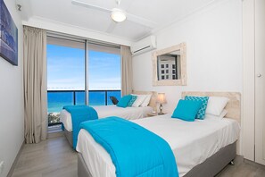 Enjoy a serene sea view from the large window in this stylish room featuring two beds and a ceiling fan.