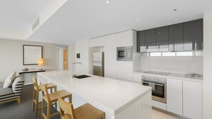 A modern kitchen with white cabinetry, a central island, stainless steel appliances, and a seating area with a sofa and chairs. - Apartment 22502. Located high on the 25th floor of this famous resort hotel (Surfers Paradise)
