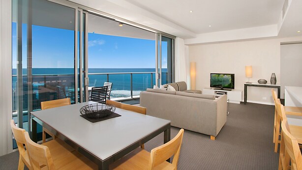A modern hotel room with a balcony, a dining area, a sofa, and a TV. - Apartment 22502. Located high on the 25th floor of this famous resort hotel (Surfers Paradise)