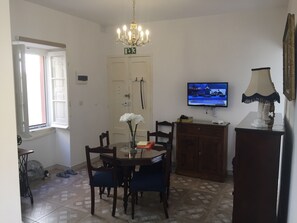 A dining area with a round table, chairs, a chandelier, a television, and a cabinet.