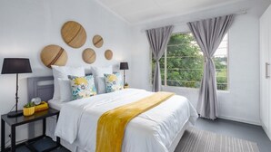 A hotel room with a large bed, two bedside tables, a window with curtains, and decorative wall hangings. - Modern Bohemian Apartment with Pool, Fibre Wi-Fi and Bbq Patio in Centurion (Centurion)
