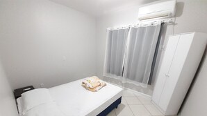 Ein kleines, sauberes Zimmer mit einem Einzelbett, einem Kleiderschrank und einem fenster mit Vorhängen.