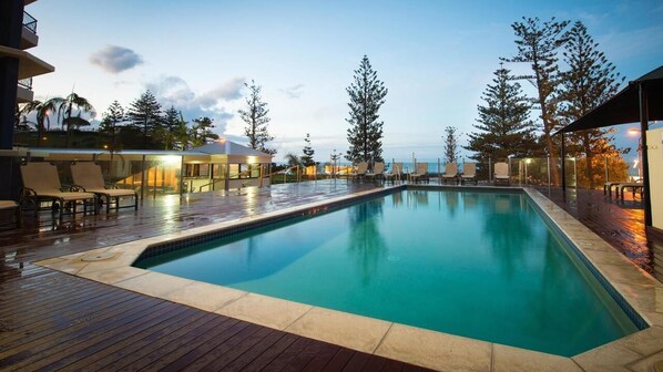 Relax by the pool surrounded by lush greenery and a wooden deck.