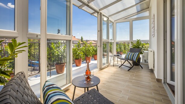 A spacious balcony with large windows, a table with a bottle and glasses, and a chair. - Enjoy your private terrace near City Park! (Budapest)