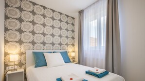 A neatly made bed with blue and white bedding, a nightstand with a lamp, and a patterned wall. - Enjoy your private terrace near City Park! (Budapest)