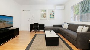 Ein modernes Wohnzimmer mit einem Flachbildfernseher, einem grauen Sofa, einem Couchtisch und einem schwarzen Bürostuhl.