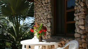A patio with a stone wall, a table, two white chairs, and a vase with flowers.