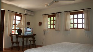 A bedroom with a large bed, a desk with a computer, and two windows with curtains.